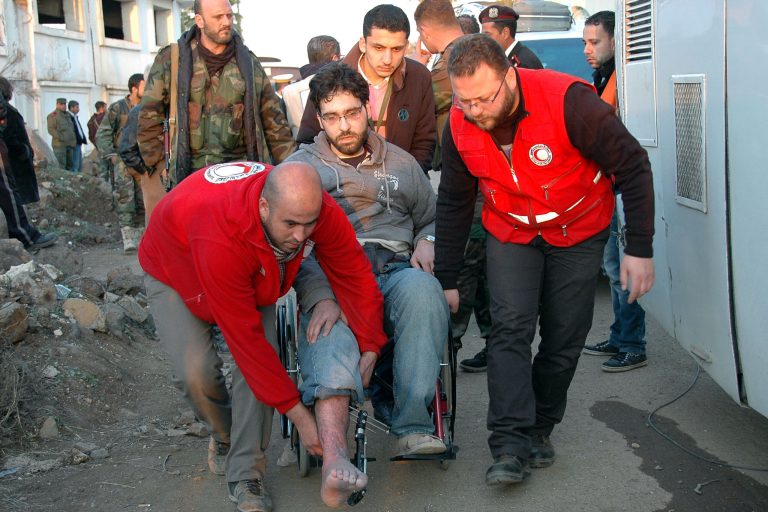 In this photo taken on Sunday Feb. 9, 2014, and released by the Syrian official news agency SANA, Syrian Arab Red Crescent members in red uniforms help evacuate an injured man on a bus out of the battleground city of Homs, Syria. A Syrian Red Crescent official says around 300 more people were evacuated Monday from besieged rebel-held neighborhoods of Syria's third-largest city, Homs. (AP Photo/SANA)