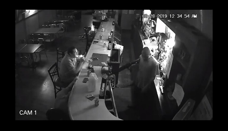 A seated man lights a cigarette while a robbery is underway at a bar in St. Louis.