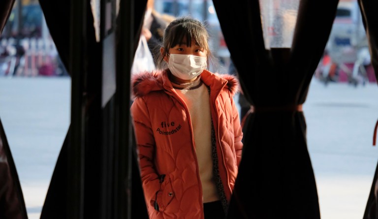 A girl wearing a face mask stands in the entrance to a shop in Wuhan in central China's Hubei Province, Friday, Jan. 31, 2020