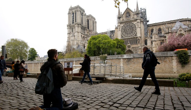 Man kneels as people came to watch and photograph the Notre Dame cathedral after the fire in Paris, Tuesday, April 16, 2019. Experts are assessing the blackened shell of Paris' iconic Notre Dame cathedral to establish next steps to save what remains after a devastating fire destroyed much of the almost 900-year-old building.