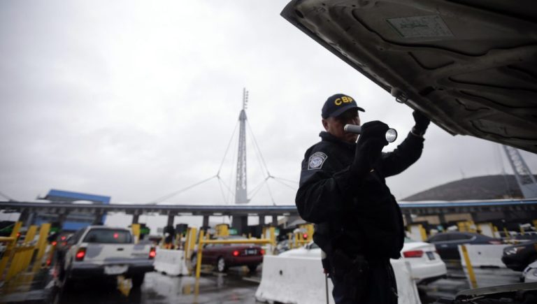A U.S. Customs and Border Protection officer checks under the hood of a car.
