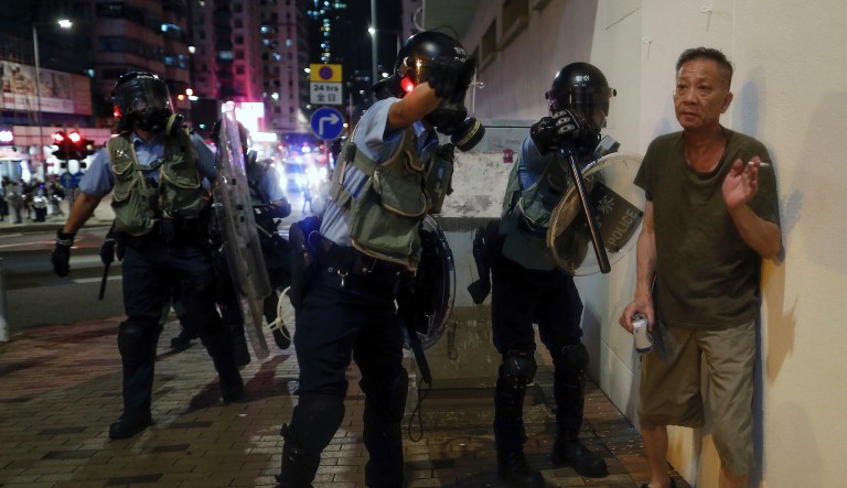 Policemen with riot gear ask a man to move as they confront protesters in Hong Kong on Wednesday, Aug. 14, 2019. German Chancellor Angela Merkel is calling for a peaceful solution to the unrest in Hong Kong amid fears China could use force to quell pro-democracy protests.