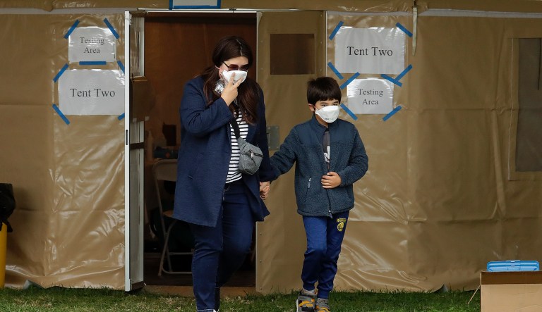 A woman grasps the hand of a child after being tested for COVID-19 on Monday, March 23, 2020, in Hayward, Calif. According to the city of Hayward, the free coronavirus testing center was launched "so sick people, first responders, and healthcare workers with recent suspected exposures to the novel coronavirus can be tested for infection." The test is free to the public, no matter where they live or immigration status. The center will have 350 kits daily, and is a partnership between the Hayward Fire Department and Avellino Lab USA, Inc., a Menlo Park gene therapy and molecular diagnostics firm that specializes in eye care medication.