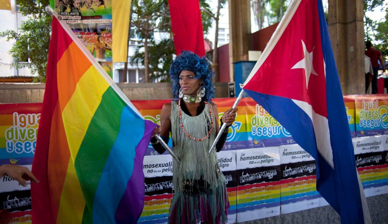 A transvestite holds a gay rights banner and a Cuban national flag while posing for photographers during celebrations marking the upcoming International Day Against Homophobia, in Havana, Cuba, Saturday, May 11, 2013. About 500 people marched through the Cuban capital to the rhythm of conga drums in an early celebration of the international day against homophobia, commemorated annually on May 17.