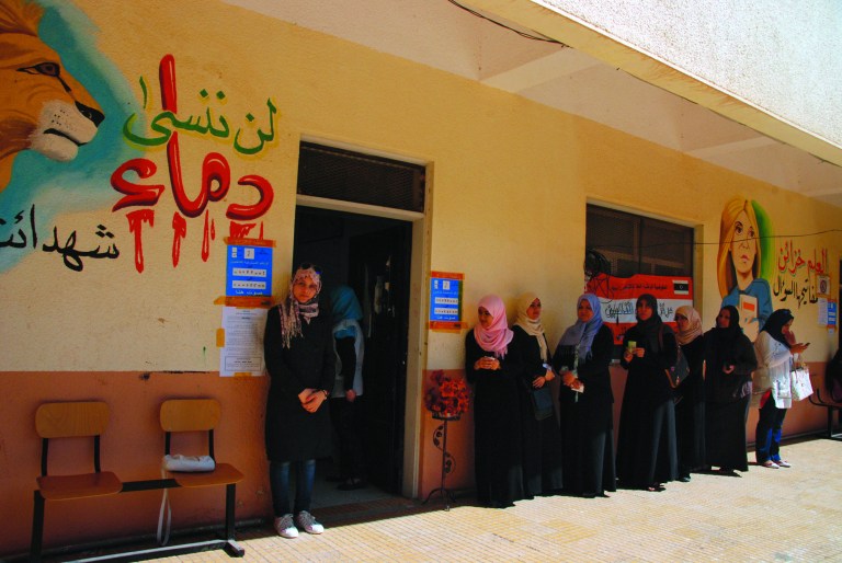 Libyan voters line up at a polling station in Benghazi, Libya Saturday, July 7, 2012. Jubilant Libyans marked a major step toward democracy after decades of erratic one-man rule, voting Saturday in the first parliamentary election after last year's overthrow and killing of longtime dictator Moammar Gadhafi. But the joy over the historic vote was tempered by boycott calls, the burning of ballots and other violence in Libya's restive east. Arabic at left reads