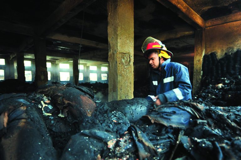 A Bangladeshi police official inspects the burnt garment factory in the Savar neighborhood outside Dhaka, Bangladesh, Sunday Nov. 25, 2012. At least 112 people were killed in a late Saturday night fire that raced through the multi-story garment factory just outside of Bangladesh's capital, an official said Sunday.(AP Photo/ khurshed Rinku)