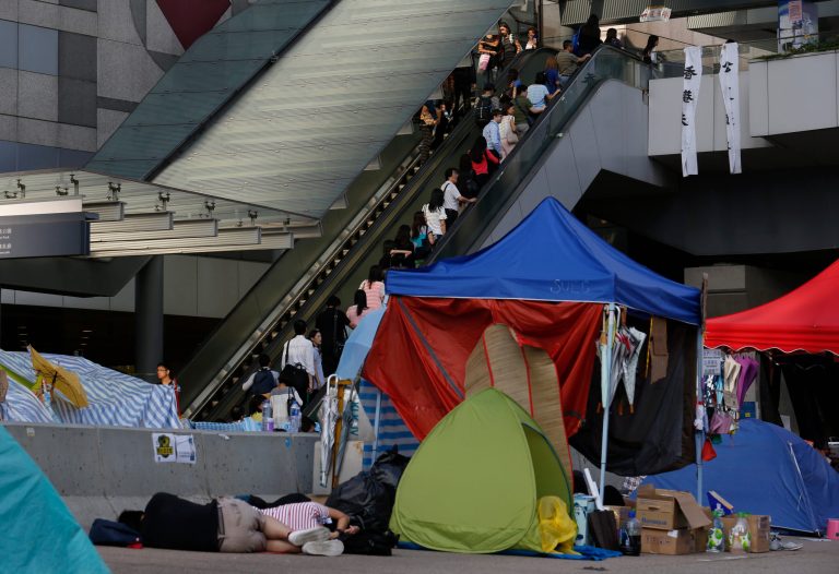 People take an escalator to head to work as the pro-democracy student protesters sleep on a roadside in the occupied areas surrounding the government complex in Hong Kong, Monday, Oct. 6, 2014. Hong Kong's civil servants returned to work and schools were reopening Monday as a massive pro-democracy protest that has occupied much of the city center for the week dwindled. (AP Photo/Kin Cheung)