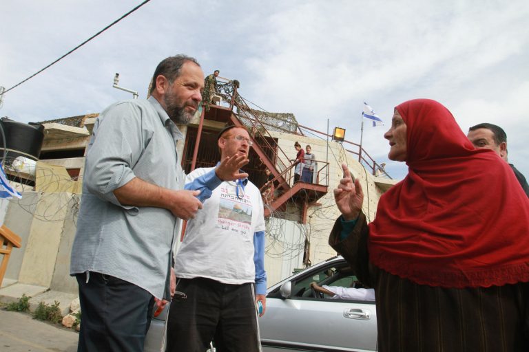 Jewish settler listen to a gesturing Palestinian woman as Jewish settler families move belongings into a contested house, seen behind, in the volatile city of Hebron after a protracted legal battle, in the West Bank city of Hebron, Sunday, April 13, 2014.  Settlers first moved into the building in 2007, but were evicted by the army amid legal issues over how they obtained the property, but they are now re-occupying the property after a court recently found the purchase of the home to be legitimate.(AP Photo/Nasser Shiyoukhi)