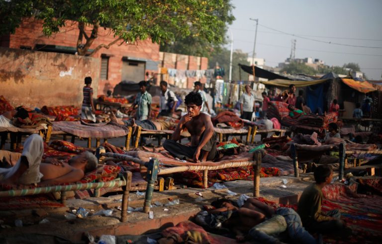 An Indian squatter smokes as others sleep on rented cots at a public park near Jama Masjid, or the Grand Mosque, in New Delhi, India, Friday, Oct. 17, 2014. The International Day for the Eradication of Poverty is observed on Oct. 17 and is designated to promote awareness of the need to eradicate poverty and destitution in the world. (AP Photo/Altaf Qadri)