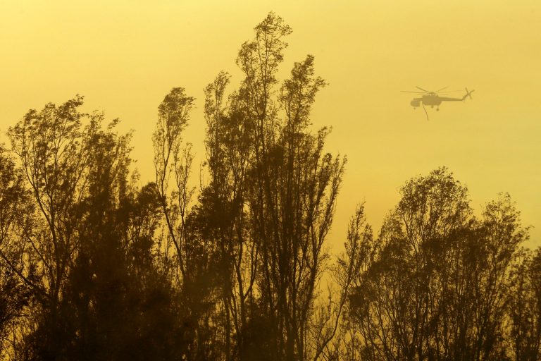 A helicopter transporting water flies over trees during a wildfire Thursday, May 15, 2014, in Escondido, Calif. One of the nine fires burning in San Diego County suddenly flared Thursday afternoon and burned close to homes, trigging thousands of new evacuation orders.(AP Photo/Gregory Bull)