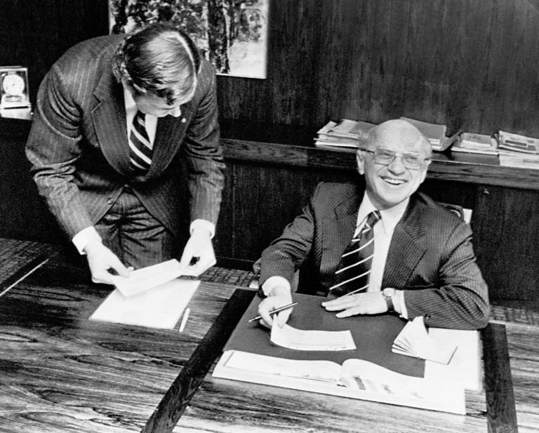 Nobel winning economist Milton Friedman receives his prize sum of $150,000 (U.S.) at PKbanken in Stockholm, from Claes G. Tisell, left, Dec. 13, 1976. (AP Photo/Reportagebild)