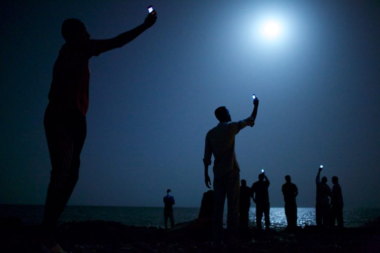 In this photo provided on Friday Feb. 14, 2014 by World Press Photo, the World Press Photo of the Year 2013 by John Stanmeyer, USA, VII for National Geographic, shows African migrants on the shore of Djibouti city at night, raising their phones in an attempt to capture an inexpensive signal from neighboring Somalia in Djibouti City, Djibouti, Feb. 26, 2013. (AP Photo/John Stanmeyer, VII for National Geographic) NO SALES NO ARCHIVE