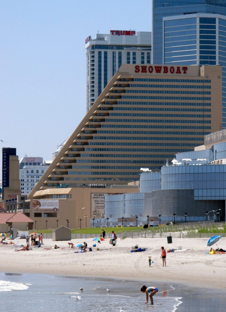 In this photo taken on July 23, 2014, people play on the beach in Atlantic City N.J., near of the Showboat Casino Hotel, center, Revel, foreground right, and Trump Plaza, background top. Showboat and Revel are expected to shutdown this weekend. Trump Plaza will close on Sept. 16. Nearly 8,000 workers will lose their jobs when the three casinos shut down. Atlantic City is planning additional job training as three casinos prepare to shut down over the next few weeks, putting thousands of workers on the street. (AP Photo/Wayne Parry)