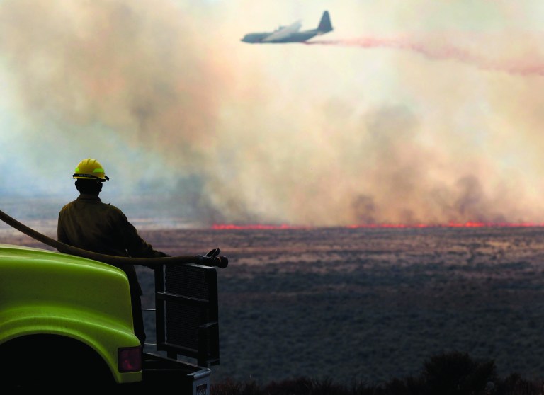 Luke Fuller, with Salmon Track Rural Fire District, watches an air tanker drop retardant on a wildfire north of Jackpot, Nev., on Tuesday, July 10, 2012. (AP Photo/The Times-News, Ashley Smith)