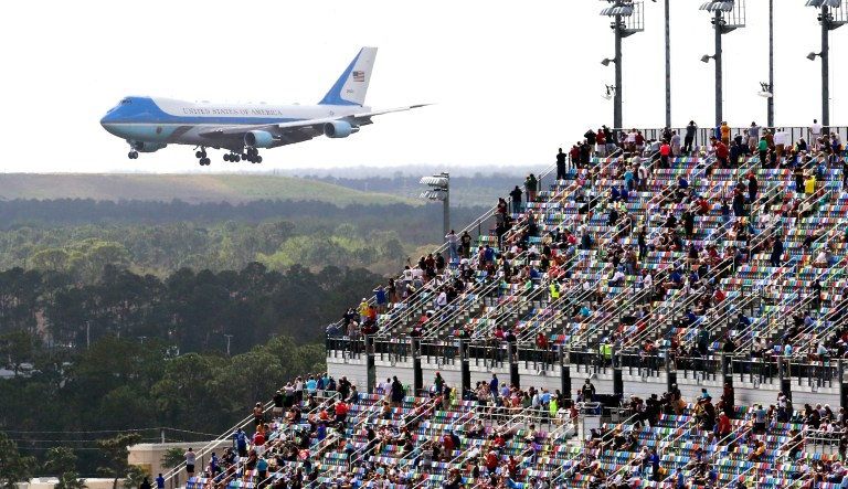 Race fans watch from the grandstands as Air Force One circles the Daytona International Speedway as President Donald Trump makes his arrival to attend the NASCAR Daytona 500 auto race at Daytona International Speedway, Sunday, Feb. 16, 2020, in Daytona Beach, Fla.