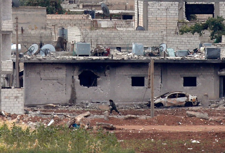 In this image shot with an extreme telephoto lens from a hilltop in Mursitpinar on the outskirts of Suruc at the Turkey-Syria border, a female Kurdish fighter runs to her position in Kobani, Syria, during fighting between Syrian Kurds and the militants of Islamic State group, Thursday, Oct. 16, 2014. Kobani, also known as Ayn Arab, and its surrounding areas, has been under assault by extremists of the Islamic State group since mid-September and is being defended by Kurdish fighters. (AP Photo/Lefteris Pitarakis)