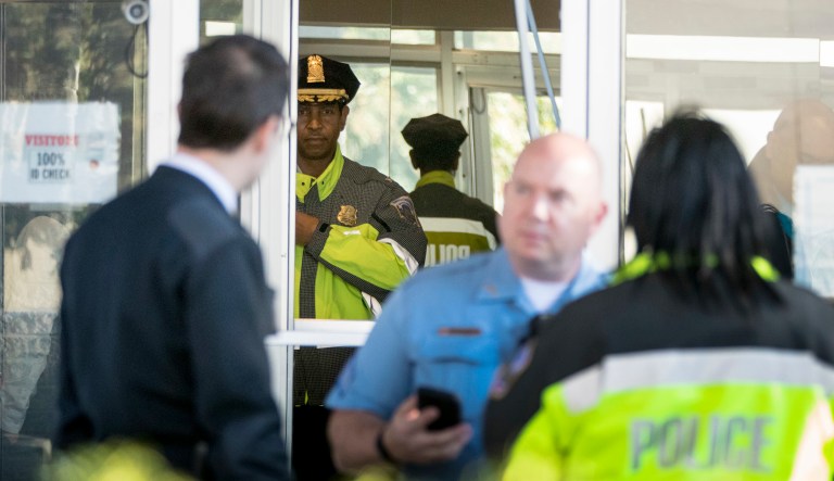 Metropolitan Police Second District Commander Melvin Gresham, second from left, accompanied by other police officers, stands at the broken front door of the offices of the local broadcast affiliate after a man was shot by a security guard while trying to break into the lobby of the building, Monday, Oct. 22, 2018, in Washington.