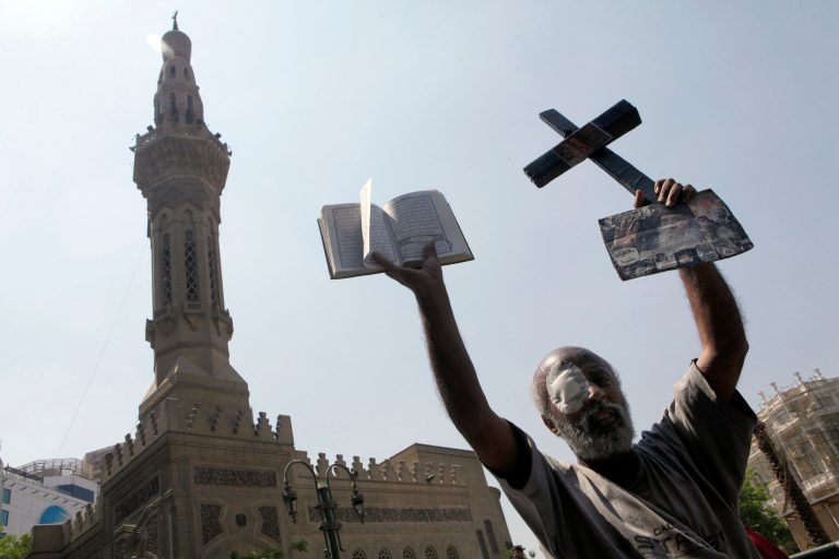 An Egyptian protester holds a cross and a copy of Islam's holy book, the Quran, during a protest in Tahrir Square, the focal point of Egyptian uprising, to condemn sectarian clashes in Cairo, Egypt, Friday, April 12, 2013. Several Christians, along with a Muslim, were killed in clashes on Saturday in a town north of Cairo. Coptic Christians make up about 10 percent of Egypt's estimated 90 million people. Attacks against Christians have increased since the ouster two years ago of autocrat Hosni Mubarak.(AP Photo/Amr Nabil)