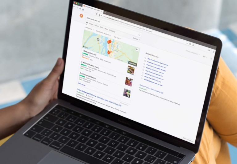 A laptop with the DuckDuckGo search engine is placed on a user's lap while sitting down.