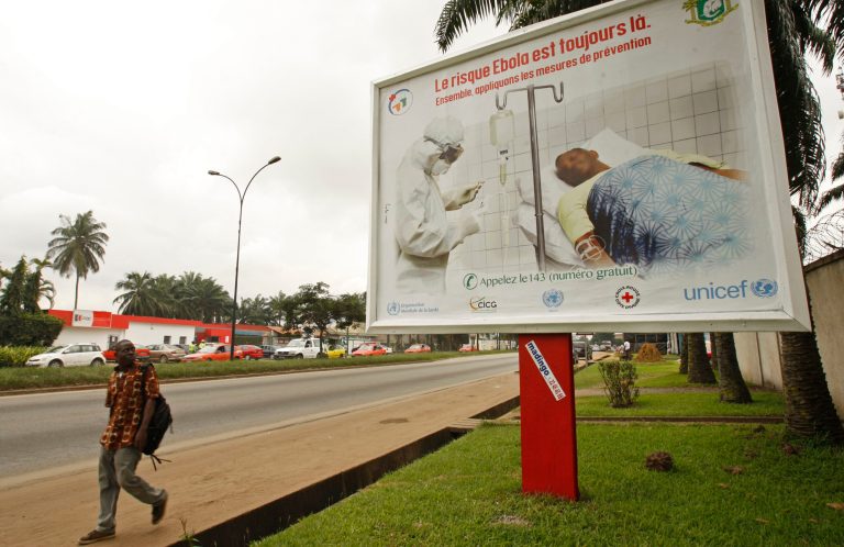 A man, left, walk past a Ebola awareness campaign poster, in the city of Abidjan, Ivory Coast,  Monday, Aug. 25, 2014. (AP Photo/Sevi Herve Gbekide )