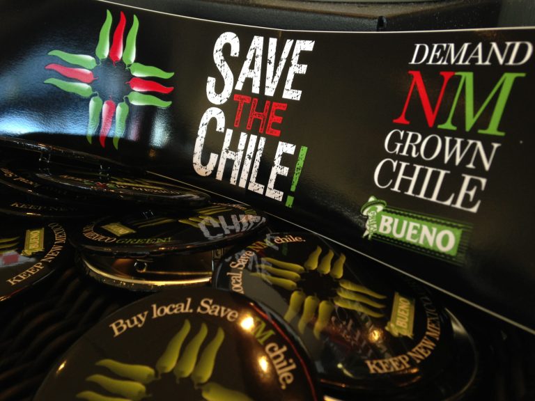 In this July 31, 2013 image, a collection of bumper stickers and buttons promoting New Mexico-grown chile sits on the order counter at Hello Deli restaurant in Albuquerque, N.M. A friendly Super Bowl bet between the mayors of Seattle and Denver has created a stir this week in New Mexico, re-energized efforts to promote the state's famous hot peppers. (AP Photo/Susan Montoya Bryan)
