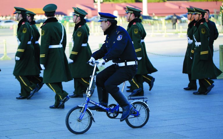 Chinese paramilitary policemen march as police officer rides a bicycle during the 18th Chinese Communist Party Congress in Tiananmen Square in Beijing, China, Tuesday, Nov. 13, 2012. (AP Photo/Lee Jin-man)