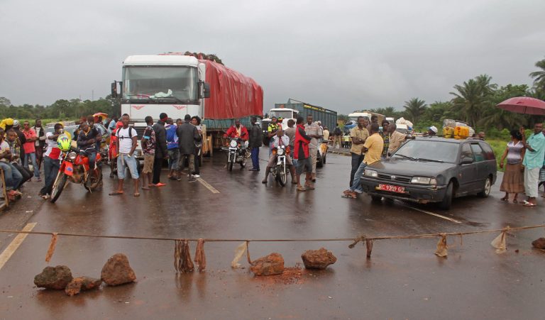 In this photo taken on Tuesday, Aug. 12,  2014, stranded people stand behind a  rope across the road that separates Guinea and Sierra Leone, and works as a makeshift border control checkpoint at Gbalamuya-Pamelap, Guinea. As Guinea closed its border with Sierra Leone at the weekend in an attempt to halt the spread of the deadly Ebola virus, people and goods were not able to cross to either side.  (AP Photo/ Youssouf Bah)
