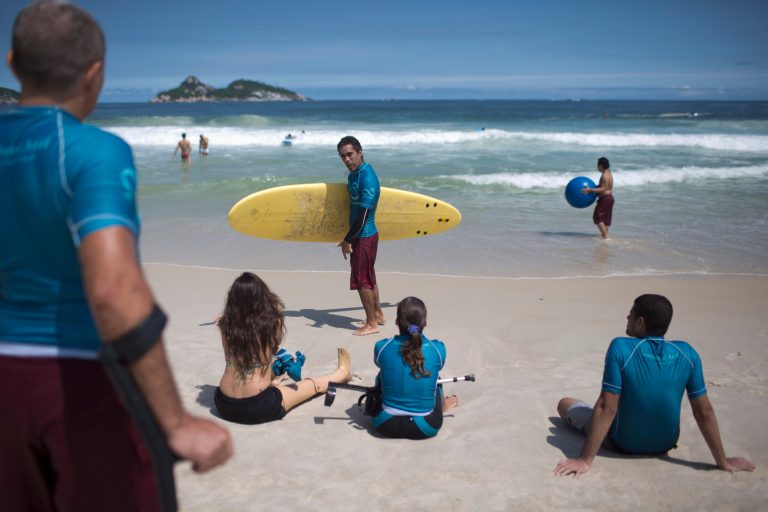In this March 16, 2013 photo, AdaptSurf co-founder and physical therapist Luiz Phelipe Nobre, center, teaches surfing lessons at Barra da Tijuca beach in Rio de Janeiro, Brazil. AdaptSurf is a Rio-based non-governmental organization that aims to make beaches accessible to the disabled and encourage them to practice water sports. (AP Photo/Felipe Dana)