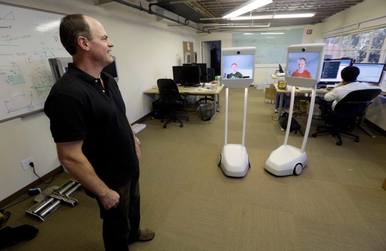   Bo Preising, Suitable Technologies' vice president of engineering, at left, talks with fellow engineers, Josh Faust, center on screen, and Josh Tyler, on screen at right, both using a Beam remote presence system in Palo Alto, Calif., Wednesday, Dec. 12, 2012. More employees are working from home, but there's still no substitute for actually being at the office. Enter the Beam. It's a roving computer screen _ with video cameras, microphones and speakers _ that stands five feet and rides on motorized wheels. (AP Photo/Marcio Jose Sanchez)  