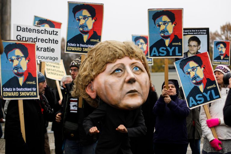 A demonstrator with a mask depicting German Chancellor Angela Merkel poses in front of other protesters holding posters of former National Security Agency NSA member Edward Snowden, outside the German Parliament in Berlin on Nov. 18. (AP Photo/Markus Schreiber)