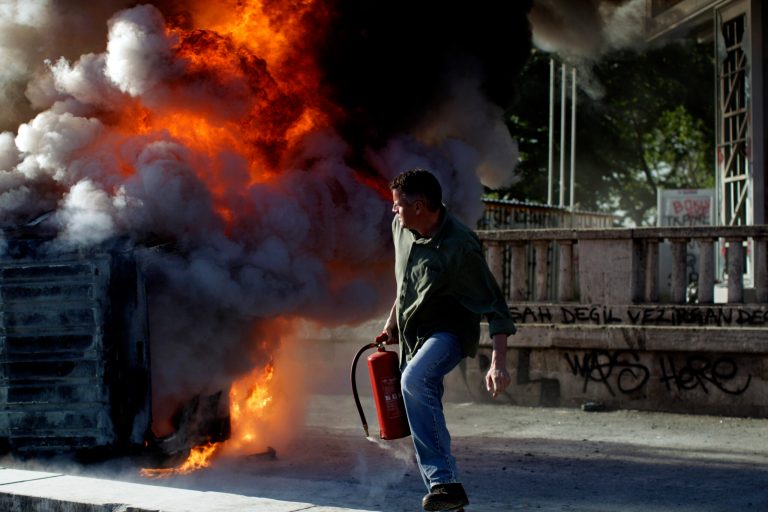A protester holding a fire extinguisher moves away from a burning car during a protest at Taksim Square in Istanbul, Monday, June 3, 2013. Demonstrations that grew out of anger over excessive police force have spiraled into Turkey's biggest anti-government demonstrations in years, challenging Prime Minister's Recep Tayyip Erdogan power. (AP Photo/Kostas Tsironis)