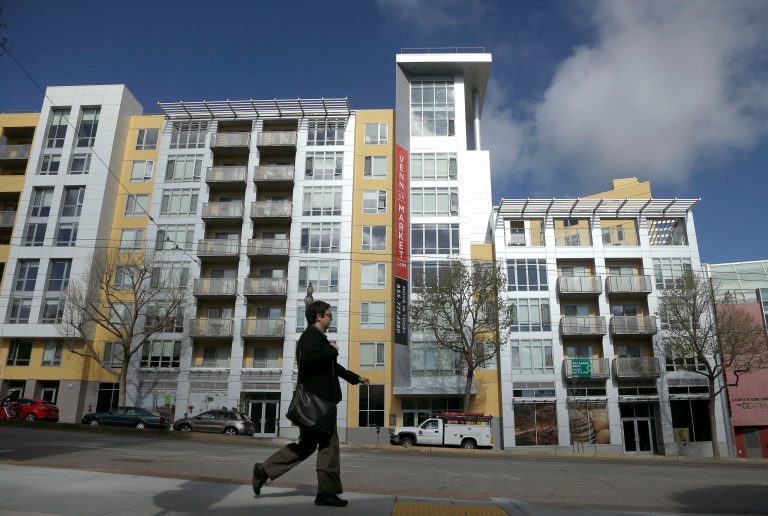 A woman walks across the street from the Venn on Market apartment and condominium building in San Francisco. (AP Photo/Jeff Chiu)
