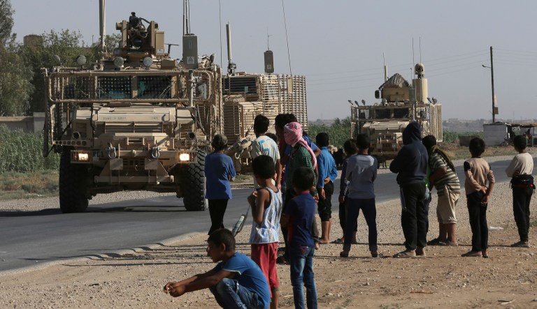 In this July 26, 2017 file photo, Syrian children and youths gather on a street as they look at a U.S. armored vehicle convoy pass on a road that links to Raqqa, northeast Syria. Officially, there are 503 U.S. troops in Syria, though the true number was widely suspected to be higher. (AP Photo/Hussein Malla, File)