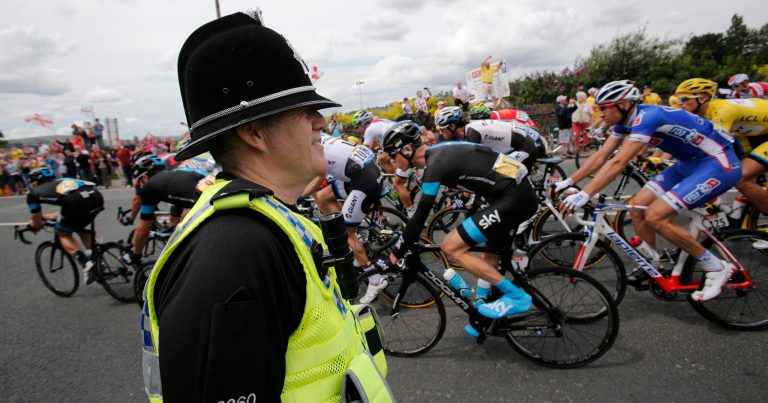 Britain's Christopher Froome, center right with race number one, passes a police officer during the second stage of the Tour de France cycling race over 201 kilometers (124.9 miles) with start in York and finish in Sheffield, England, Sunday, July 6, 2014. (AP Photo/Christophe Ena)