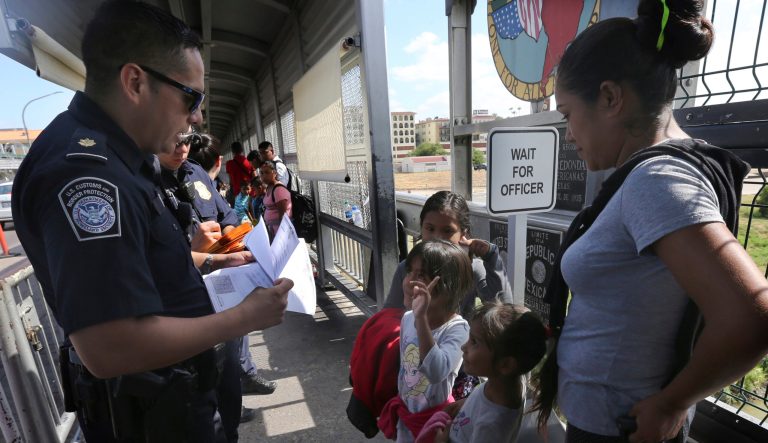 A United States Customs and Border Protection Officer checks the documents of migrants, before being taken to apply for asylum in the United States.