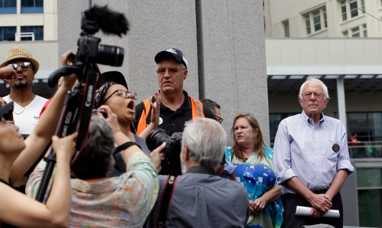 A protestor continues to speak while surrounded by media members as Democratic presidential candidate Sen. Bernie Sanders, I-Vt., looks on at right before leaving the stage at a rally Saturday, Aug. 8, 2015. (AP Photo/Elaine Thompson)