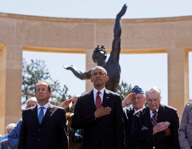 U.S. President Barack Obama, centre, and French President Francois Hollande, left,  stand with veterans during the playing of Taps, at Normandy American Cemetery at Omaha Beach as he participates in the 70th anniversary of D-Day in Colleville sur Mer, Normandy, France, Friday, June 6, 2014. (AP Photo/Charles Dharapak)