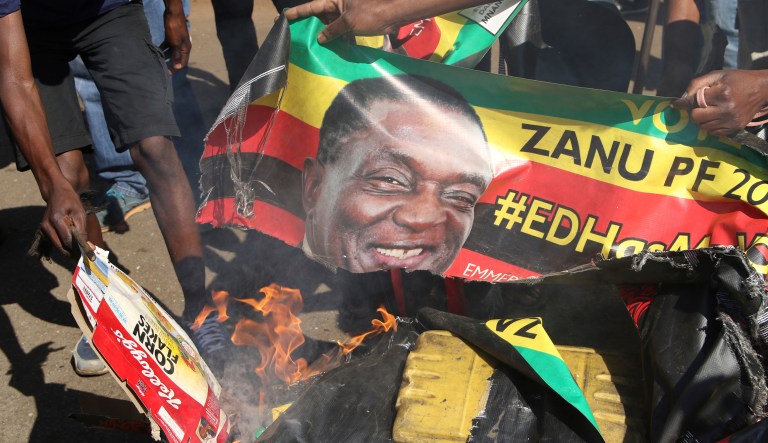 Opposition MDC party supporters burn election posters with  Zimbabwean President Emmerson Mnangagwa during protest in the streets of Harare Wednesday, Aug. 1, 2018. Hundreds of angry opposition supporters outside Zimbabwe's electoral commission were met by riot police firing tear gas as the country awaited the results of Monday's presidential election, the first after the fall of longtime leader Robert Mugabe.