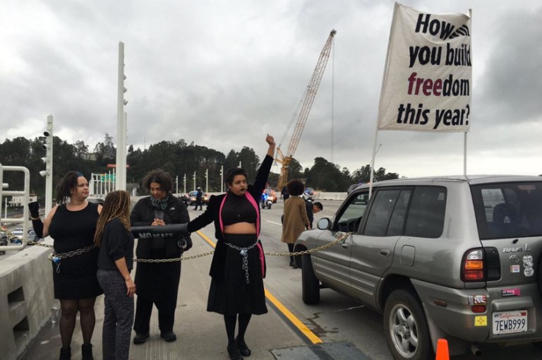 Activists sporting Black Lives Matter shirts and signs, chaining themselves and several cars along the width of the Bay Bridge bridge pass. (Photo courtesy of the Twitter account of BrownBlaze)