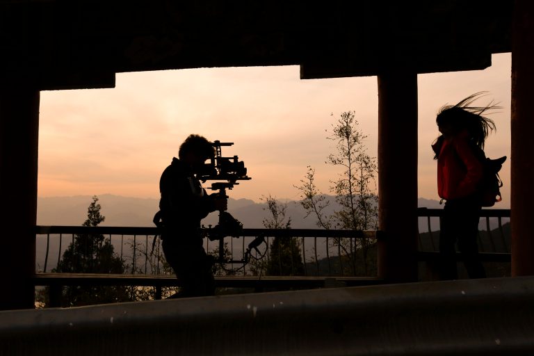 In this Oct. 20, 2013 photo, a cameraman, left, stabilizes his camera to film an actress walking through a wooden corridor on the top of a mountain for a set of an online microfilm on the outskirts of Beijing. Chinese authorities are requiring makers of online films to gain licenses and report their content before it is posted, tightening regulation of what in recent years has been a more freewheeling genre than China's traditional film industry. (AP Photo/Alexander F. Yuan)