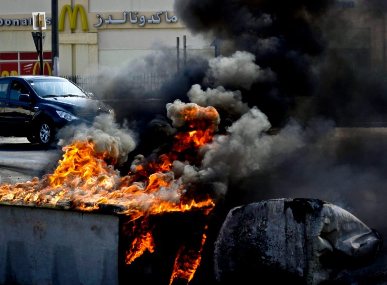   Vehicles pass by tires and old water storage tanks set on fire by Bahraini anti-government protesters in Malkiya, Bahrain, Monday, Dec. 17, 2012. Pro-democracy protests continue in villages around the Gulf island kingdom. (AP Photo/Hasan Jamali)  