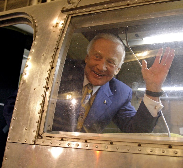 Col. Buzz Aldrin, former Apollo 11 lunar module pilot, waves from inside a NASA Mobile Quarantine Facility, identical to the one he spent time in immediately upon his return from his voyage to the moon. (AP Photo/Ben Margot)