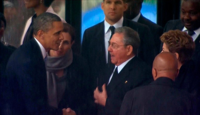 US President Barack Obama shakes hands with Cuban President Raul Castro at the FNB Stadium in Soweto, South Africa, in the rain for a memorial service for former South African President Nelson Mandela, Tuesday. (AP/SABC Pool)
