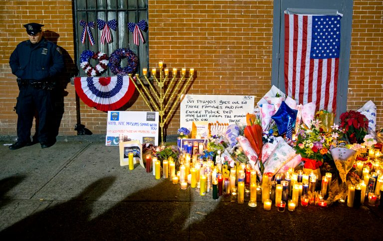 A New York City police officer stands near a growing memorial Sunday, Dec. 21, 2014, near the spot where two New York Police Department officers, sitting inside a patrol car the previous day, were shot by an armed man, killing them both. (AP Photo/Craig Ruttle)