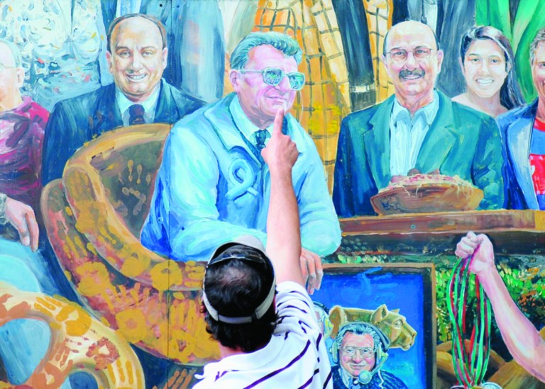 A visitor points to the spot in a mural by Michael Pilato where a halo that was above the late Penn State football coach Joe Paterno has been painted over by the artist in State College, Pa. on Saturday, July 14, 2012. Pilato had put a halo over Paterno's image after the beloved coach's death in January, but said he felt he had to remove it Saturday after a report that Paterno, former university president Graham Spanier and others buried allegations of child sex-abuse against ex-assistant Jerry Sandusky. Paterno's family denies the claim. (AP Photo/Centre Daily Times, Abby Drey)