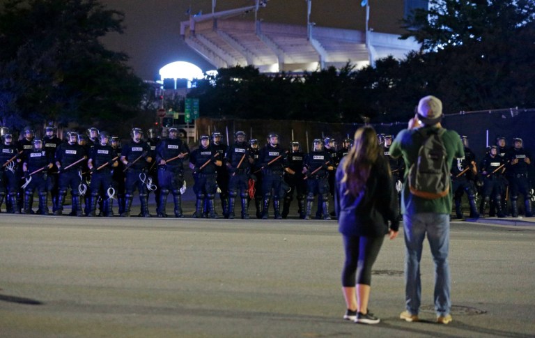 A couple looks at line of police officers blocking the access road to I-277 on the third night of protests in Charlotte, N.C. Thursday, Sept. 22, 2016, following Tuesday's fatal police shooting of Keith Lamont Scott in Charlotte, N.C. (AP Photo/Chuck Burton)