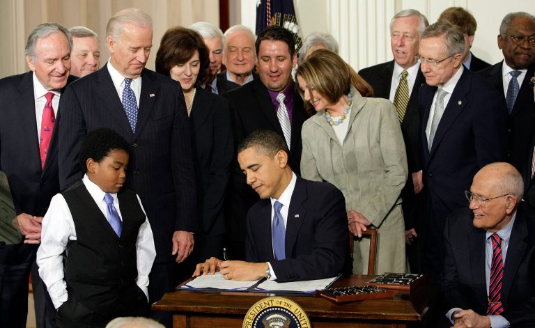   FILE - In this March 23, 2010 file photo, Marcelas Owens of Seattle, left, Rep. John Dingell, D-Mich., right, and others, look on as President Barack Obama signs the health care bill in the East Room of the White House in Washington. (AP Photo/J. Scott Applewhite, File)  