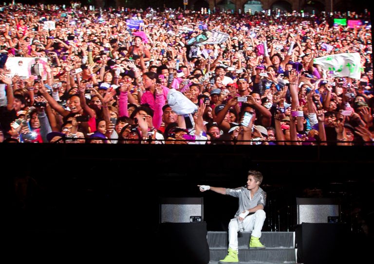   Sitting under a video screen that displays people attending his show, pop star Justin Bieber performs during a free open-air concert in Mexico City, Monday, June 11, 2012. (AP Photo/Alexandre Meneghini)  
