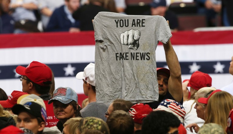 A Trump supporter holds up a T-shirt blasting "fake news" so media could see before a rally address by President Donald Trump Thursday, Oct. 4, 2018, in Rochester, Minn.