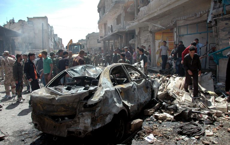 Syrian people gather at the site of one of two car bombs that exploded in the pro-government district of Zahra in the central Syrian city of Homs, Syria on April 29. (AP/SANA)